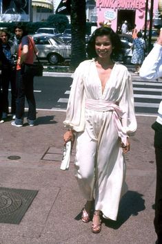 a woman is walking down the street in a white jumpsuit