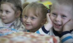 three young children sitting at a table with a cake in front of them and smiling