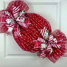 a red and white wreath hanging on the front door with ribbons tied around it's sides