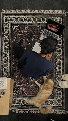 a woman laying on top of a rug next to an orange cat and laptop computer