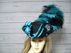 "Black woolen pirate hat/tricorn with black and turquoise ostrich feathers, turquoise pleated trim, black satin cocarde with a turquoise sparkly jewel center and two turquoise satin bows. Sooo pretty! This hat is 22.5\" for the inside circumference with a built-in hat sizer. Just cinch and tie. Please measure your head as I cannot make the circumference bigger so please keep that in mind. This is not an oversized brim pirate hat. The upturn brim is about 4\". Check out my other pirate hats and other goodies in my etsy shop. Thank you for stopping by. Have a great day. I ship Priority mail. I ship many times a week. If you need your item quicker let me know your zip code and I can figure shipping rates for you. Please let me know if you have any questions I accept Paypal, credit cards and e Blue Costume Hat For Carnival, Themed Blue Costume Hats And Headpieces, Tricorn Hat, Pirate Hat, Red Hat Society, Satin Noir, Pirate Hats, Costume Hats, Ostrich Feathers