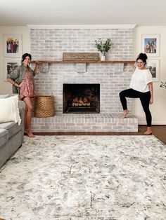 two women standing in front of a brick fireplace