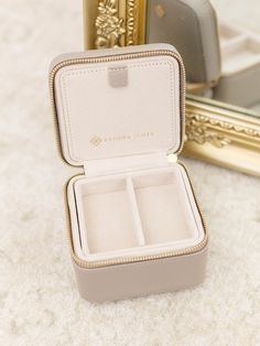 an open jewelry box sitting on top of a white carpet next to a gold framed mirror