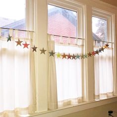 two windows with stars hanging from them in front of the window sill and curtains