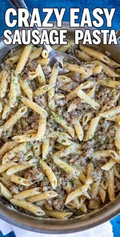 a skillet filled with sausage pasta and sauce on top of a blue table cloth