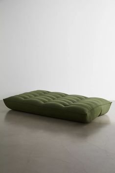 a green mattress sitting on top of a cement floor next to a white wall in an empty room