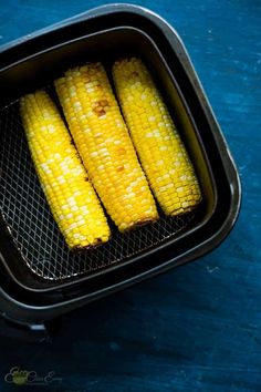 corn on the cob in an air fryer with a blue tablecloth behind it