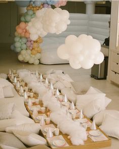 a table topped with lots of white balloons and small candles on top of wooden trays