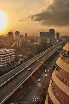 the sun is setting over a city with tall buildings and cars driving on the road