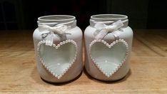 two white heart - shaped vases with bows and pearls are sitting on a table