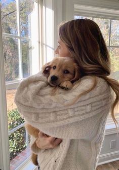 a woman holding a dog in her arms by a window with the sun shining through it