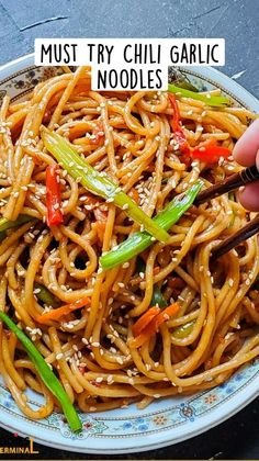 someone is holding chopsticks over a plate of noodles with sesame seeds and peppers