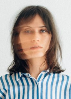 a woman with long hair wearing a blue and white striped shirt looking at the camera