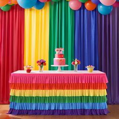 a table topped with a rainbow cake and balloons