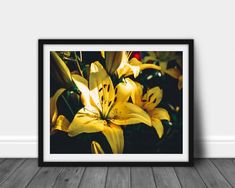 a framed photograph of yellow lilies in a room with wood flooring and white walls