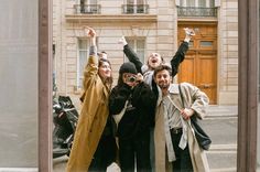 three people standing in front of a building with their arms up and one person taking a selfie