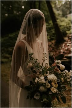 a woman in a wedding dress holding a bridal bouquet and veil over her head