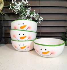 three bowls with snowmen painted on them and flowers in the vases behind them