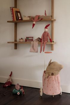 a teddy bear in a stroller next to bookshelves and toys on the floor