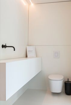 a white toilet sitting next to a wall mounted faucet in a bathroom under a light