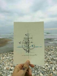 someone holding up a piece of paper with a drawing on it in front of the ocean