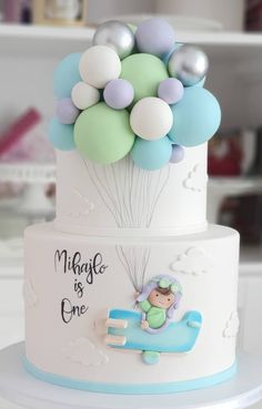 a three tiered cake decorated with balloons and a baby's first birthday card