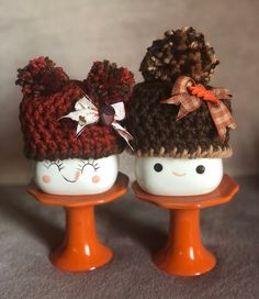 two crocheted hats are sitting on top of an orange stand, one has a bow