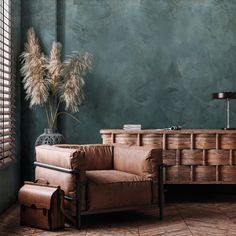 a brown chair sitting next to a wooden dresser with a vase on top of it