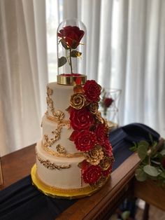 a three tiered wedding cake with red roses on top and gold trimmings