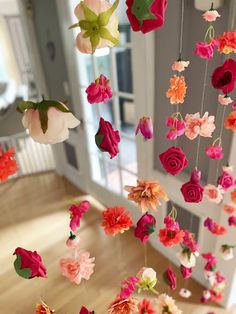 an arrangement of flowers hanging from strings in a room with wooden flooring and white walls