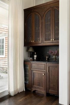 a kitchen with wooden cabinets and black counter tops next to a white curtained window