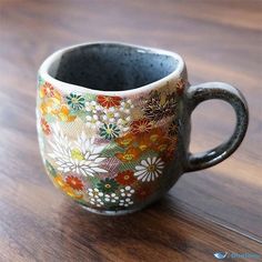 a coffee cup sitting on top of a wooden table with flowers painted on the side