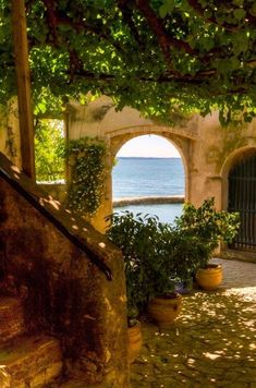 an arched doorway leads to the water and greenery in this stone walled courtyard with steps leading up to it