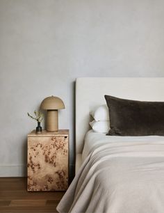 a white bed sitting next to a night stand on top of a hard wood floor