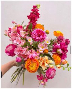 a person holding a bouquet of flowers in front of a white wall with pink, orange and yellow flowers