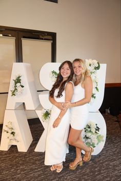 two beautiful young women standing next to each other in front of a large letter sign