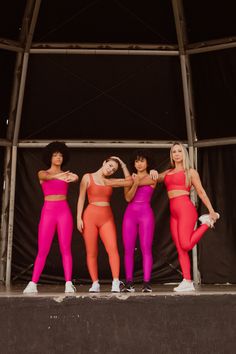 four women in bright colored outfits standing on stage with their arms around each other's shoulders