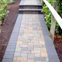 a brick walkway with steps leading up to flowers and trees in the background, surrounded by greenery