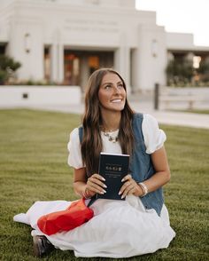 a woman sitting on the grass holding a book