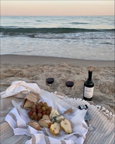 a bottle of wine and some food on a towel at the beach with two glasses of wine