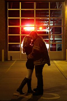 a man and woman kissing in front of a building at night with the lights on