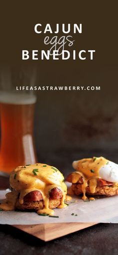 two sausages covered in cheese and sauce on top of paper next to a glass of beer