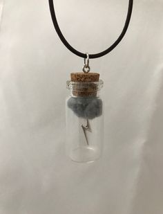 a necklace with a glass bottle filled with rocks and a silver lightning bolt on it