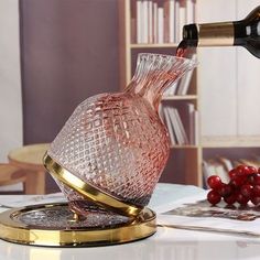 a wine bottle being poured into a glass vase on top of a table with red berries