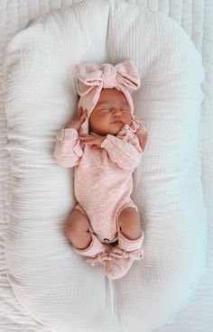 a baby is laying down on a white blanket and wearing a pink bowknoted outfit