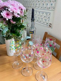 three wine glasses sitting on top of a table next to a vase filled with flowers