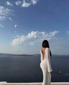 a woman in a white dress looking out over the ocean