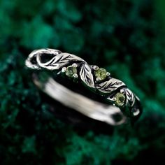 a silver ring with leaves and green stones on the inside, sitting on a mossy surface