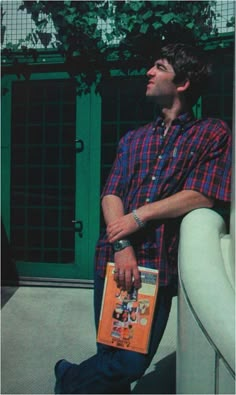 a man is sitting on a ledge holding an orange book