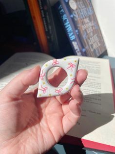 a person is holding a small ring with pink bows on it and reading a book in the background